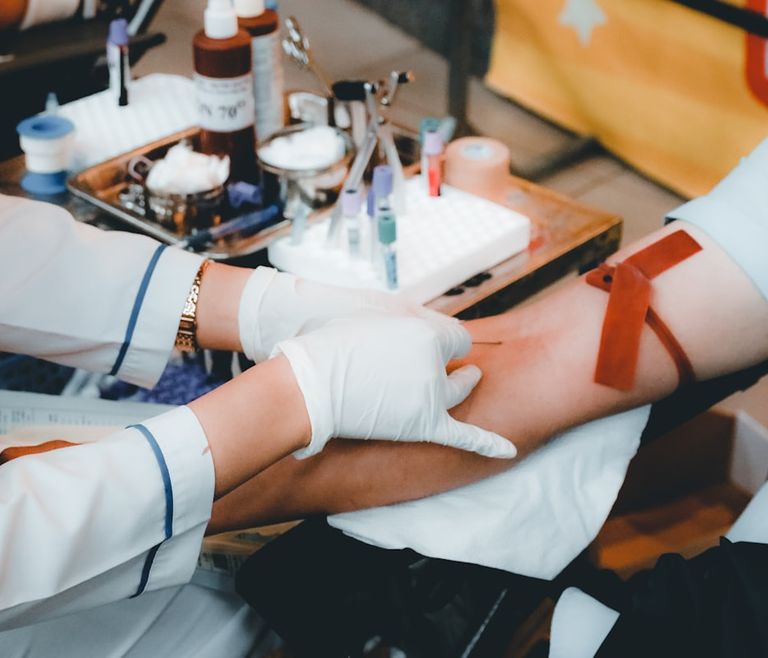 Profissional de saúde realizando coleta de sangue no braço de um paciente em sala de coleta
